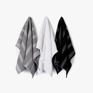 Soft and absorbent striped towels in grey, white, and black hanging on a white background. Perfect for bathroom decor and everyday use.